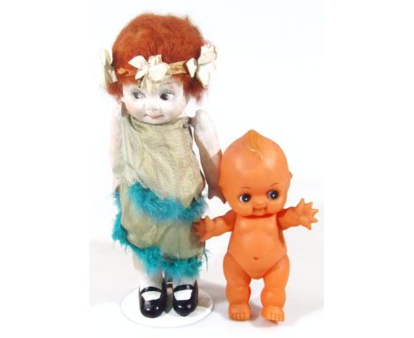 A 1920s Kewpie style doll, formed as a girl with ginger hair, articulated arms and green and gilt dress, wearing shoes, on st