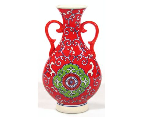 A Chinese pottery vase, the trumpet stem flanked by 'C' scroll handles, of tear drop outline decorated with flowers on a red 