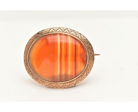 A YELLOW METAL AGATE BROOCH, of an oval form, set with a banded orange agate, collet set with a Aztec pattern  surround, stam
