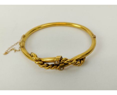 A YELLOW METAL BANGLE, probably high carat gold, set with two seed pearls, with a rope-twist cross-over design, 6cm diameter,