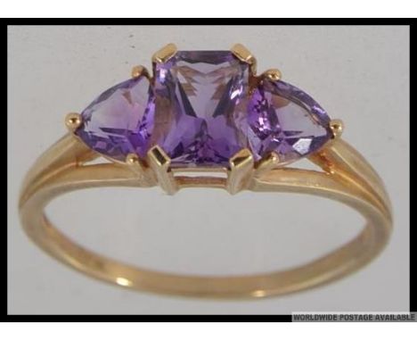 A hallmarked 9ct gold dress ring with triple stone  Amethyst in a prong setting with raised pierced shoulders. Size R.5 Weigh