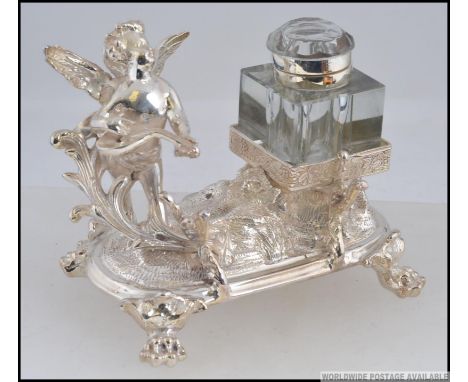 A silver plated desk set, having a pen holder  in the form of a cherub playing a string instrument, with a glass hinged ink p