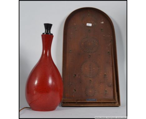A vintage wooden Corinthium bagatelle board together with a red laquered table lamp. Measures: 76cm H.