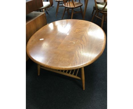 An oval Ercol coffee table in light elm, resting on turned beech legs and magazine under rack.