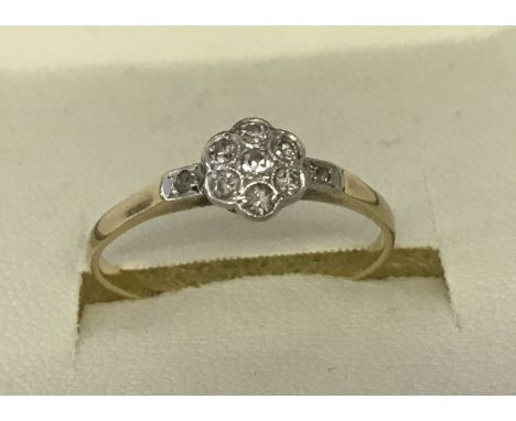 A diamond set 18ct gold and platinum dress ring of flower head design. Small central round cut diamond surrounded by 6 small 