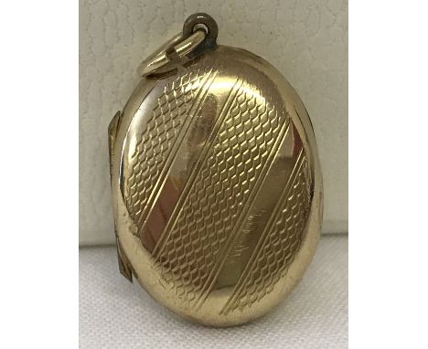A 9ct gold oval locket with engine turned decoration to front. Approx. 3cm x 1.75cm including bale. Marked 9ct with makers in
