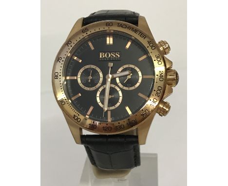 A men's modern chronograph wristwatch by Hugo Boss. Gold tone case with black leather strap. Luminescent hands with gold tone