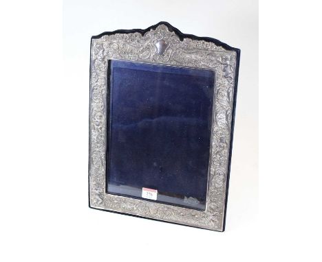 A large Victorian style silver clad easel photo frame, the whole relief decorated with cherubs, flowers and C-scrolls, having