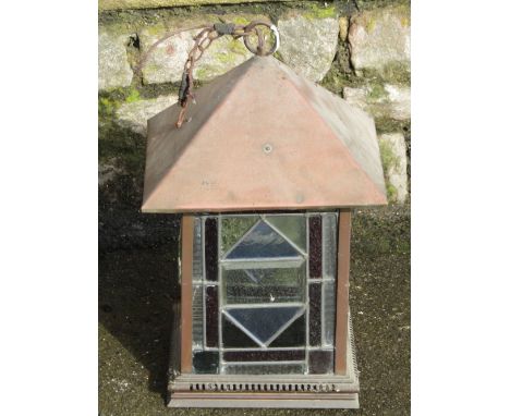 An arts and crafts style copper hall or porch lantern, of square form, enclosing coloured leaded light segmented panels, bene