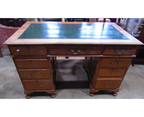 An early 20th century oak kneehole twin pedestal writing desk with inset writing surface over an arrangement of nine frieze d