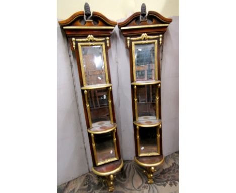 A pair of decorative wall mounted columns, mirror backed supporting three demi-lune shelves beneath a broken architectural pe