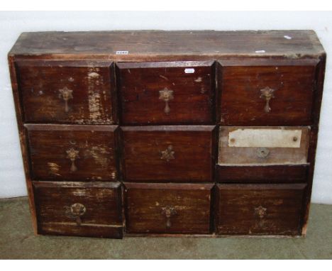 A vintage stained pine frame nest of nine drawers, presented in rows of three, 85cm wide x 20cm deep x 61cm high