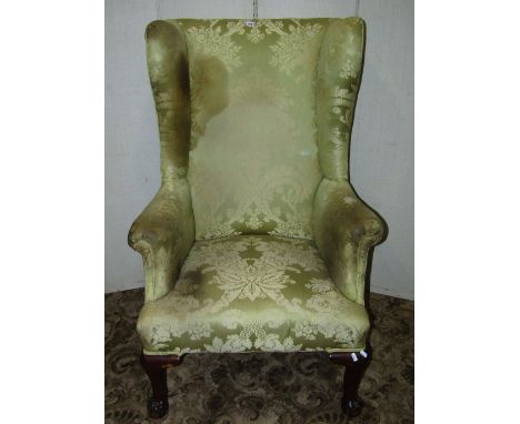 A Georgian style wing armchair with light green ground floral patterned upholstery, raised on claw and ball forelegs