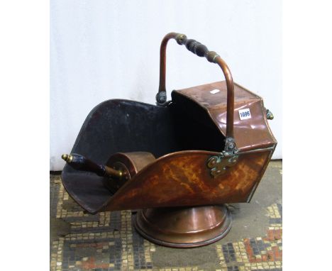 A 19th century copper helmet shaped coal scuttle with turned wooden hand grips together with associated shovel