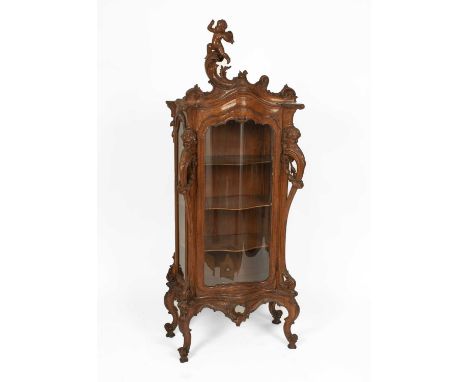 An Italian Baroque-style carved walnut display cabinet, the scrolling crest with a cherub carved crest, above a serpentine gl