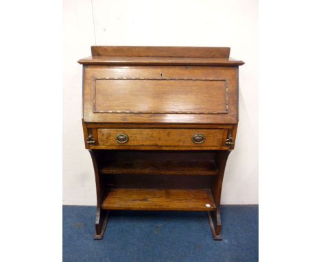 A 1930s narrow oak bureau, with beaded ecoration, and open shelf base 106cm H