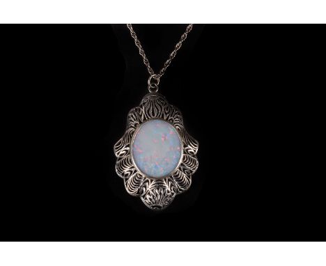 An opal pendant,  the oval stone with black enamel verso, in a  white metal open work mount, 45mm long, on a chain