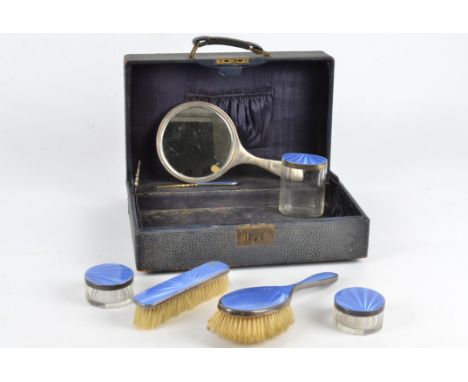 A hallmarked silver and blue enamel dressing table set,  in a case, including two brushes, a mirror, three silver topped jars