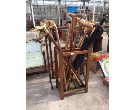 AN OAK STICK STAND WITH AN ASSORTMENT OF UMBRELLAS AND WALKING STICKS TO INCLUDE ONE WITH A SILVER COLLAR AND ONE WITH A BRAS