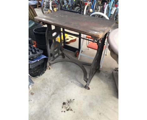 A VINTAGE WOODEN TABLE WITH HEAVY CAST IRON FOUR WHEELED BASE 