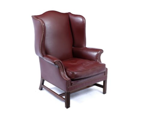 A GEORGIAN STYLE RED LEATHER UPHOLSTERED WING BACK ARMCHAIR with studded upholstered, scrolling arms and squab cushion and st