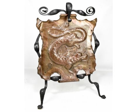 An Arts and Crafts iron framed fire screen with copper central panel relief decorated with a dragon, with easel back stand, h