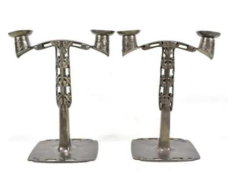 ARCHIBALD KNOX FOR TUDRIC PEWTER AND LIBERTY & CO; a pair of candelabra, with relief and pierced floral decoration raised on 