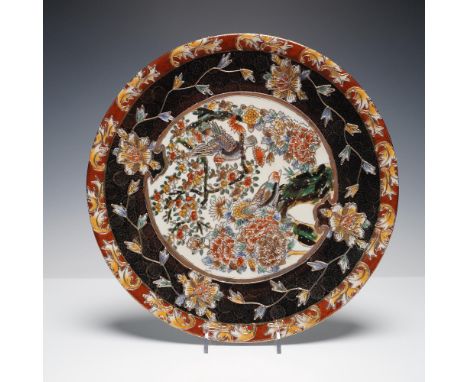 A large and richly decorated porcelain charger featuring a vibrant relief design of birds among flowering branches, framed by