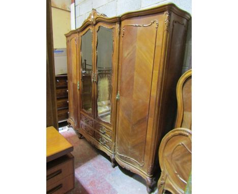 A large French triple wardrobe enclosed by four door and four drawers with carved outline raised on scrolled supports with in