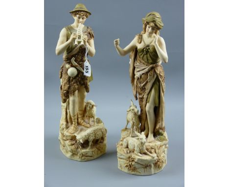 A pair of Royal Dux figures of shepherd and shepherdess, the man playing pan pipes with sheep at his feet, the girl with goat