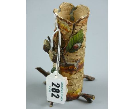 A cold painted metal vase in the form of a hollow tree trunk with protruding leafy twigs and branches, one leaf with addition