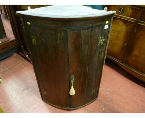 An antique crossbanded oak two door bow front hanging wall cupboard with brass hinges and escutcheon with interior shelves, 9