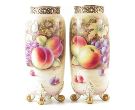 Pair of Royal Worcester vases signed T. Nutt, painted with fallen fruit below pierced rims, raised on four scroll feet, black