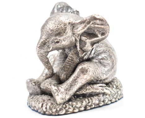 A hallmarked silver baby elephant figure. The juvenile elephant depicted sitting with ears folded back, a lowered trunk &amp;