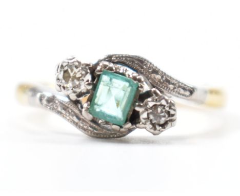 A 18ct gold &amp; platinum, emerald &amp; diamond crossover ring. The ring set with an emerald cut emerald flanked by two ill