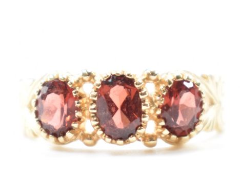 A hallmarked 9ct gold and garnet three stone ring. The ring being set with three oval cut garnets with pierced heart shaped s