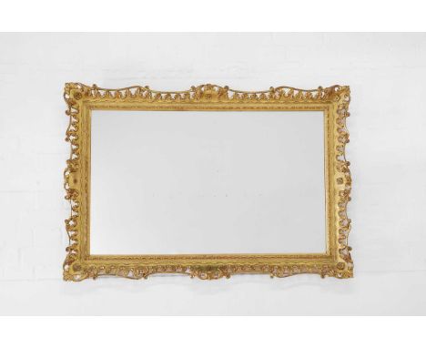 A giltwood and gesso picture-frame mirror, late 19th century, of shaped rectangular outline, the pierced rococo frame decorat