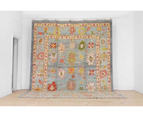 A large Oushak wool carpet,  of recent manufacture, decorated with multicoloured stylised motifs to a pale blue ground, withi