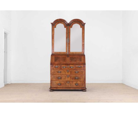 A Queen Anne walnut and feather-banded bureau bookcase, c.1710, with a double-arched top, above a pair of doors enclosing a f