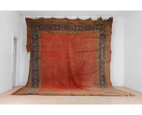 An Oushak wool carpet, early 20th century, Turkish, the vacant red field within a stepped border woven with geometric foliate