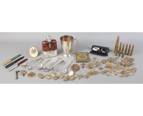 A large assortment of collectables, to include fountain pens, hip flask, silver teaspoon, military badges and brass cases.  