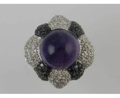 A white metal, white and black diamond, and amethyst dress ring of quatrefoil form, set central cabochon amethyst.