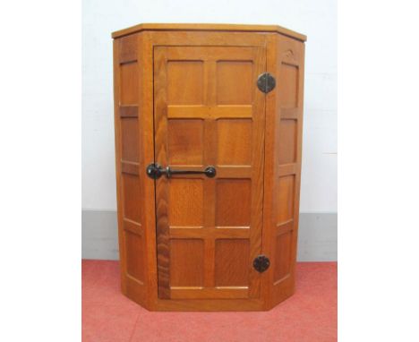 A Robert Thompson (Mouseman) Oak Hanging Corner Cupboard, with panelled door enclosing three shelves, wrought iron hinges and