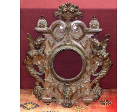 A carved oak frame with baskets of flowers finial and border of winged caryatids, 81cm x 69cm