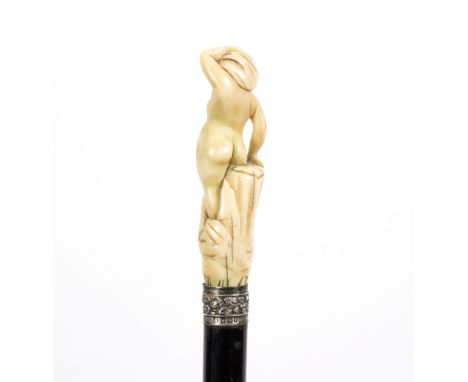 An ebonised walking stick, the 18th Century carved ivory handle in the form of a standing nude, with later silver mount/see i