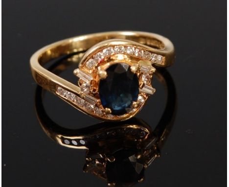 A modern 18ct gold sapphire and diamond cluster ring arranged as a four claw set oval cut sapphire in a surround of channel s