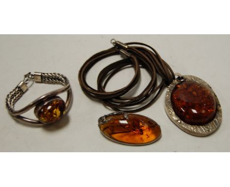 A ladies amber set bangle, in white metal mount, with ropetwist strap; together with two other amber set pendants (3)