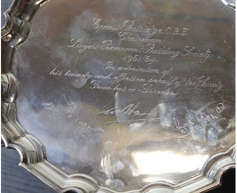 A silver circular salver, by Mappin &amp; Webb Ltd, assayed Sheffield 1963, having scroll border, raised upon triple hoof sup