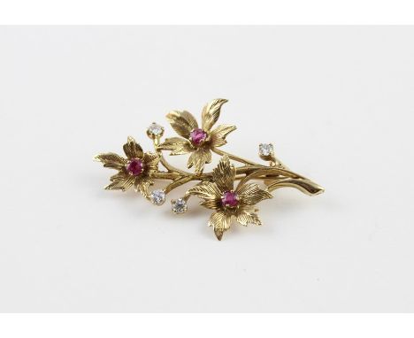 A 9ct. yellow gold, ruby and diamond brooch, fashioned as three flowers upon a stem, each having five petals with serrated ed