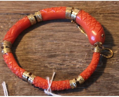 A late 19th century precious yellow metal mounted carved coral "snake" bangle, fashioned from six graduated and curved red co